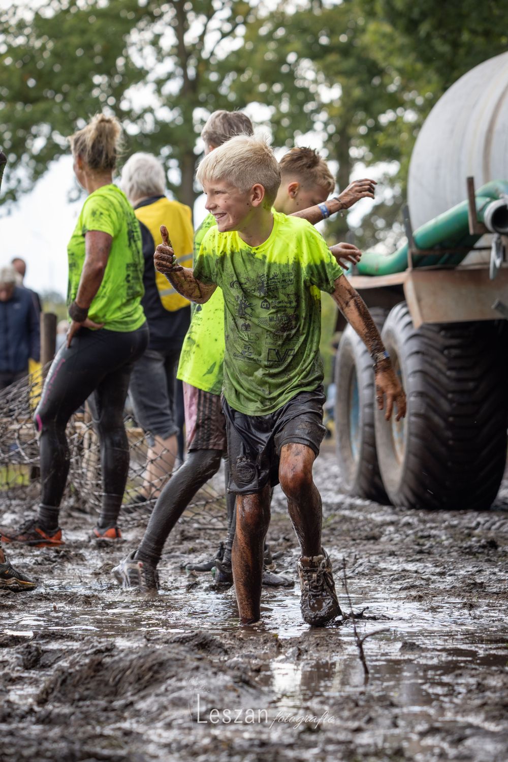 Participants in bright yellow shirts crawl through thick mud during an outdoor obstacle course event.