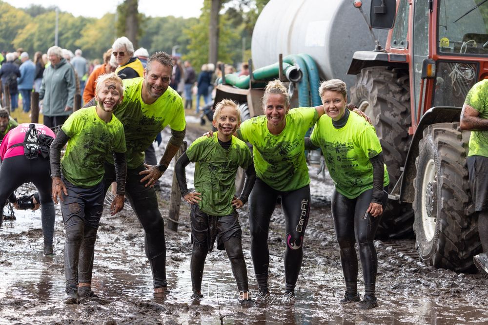 A group of people in bright yellow safety vests lean forward while participating in a muddy outdoor activity.