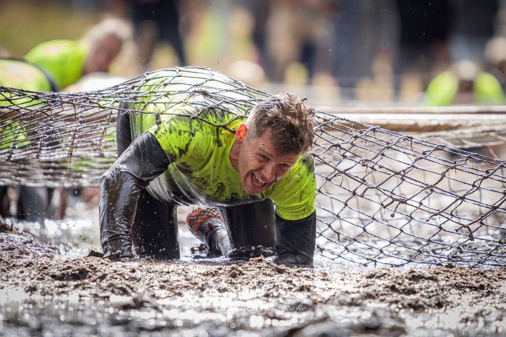 Participants crawl under barbed wire obstacles during an intense mud run competition.