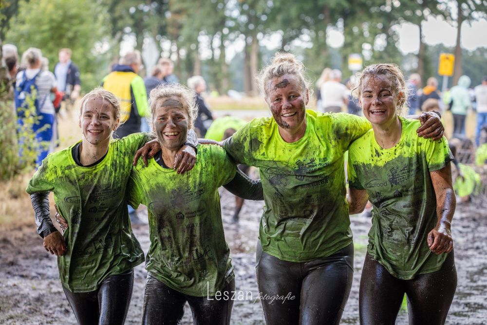 A group of participants covered in mud smile together during an outdoor obstacle course event.