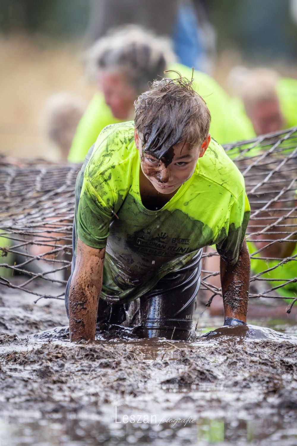 A participant in a bright yellow shirt crawls through thick mud during an obstacle course race event.
