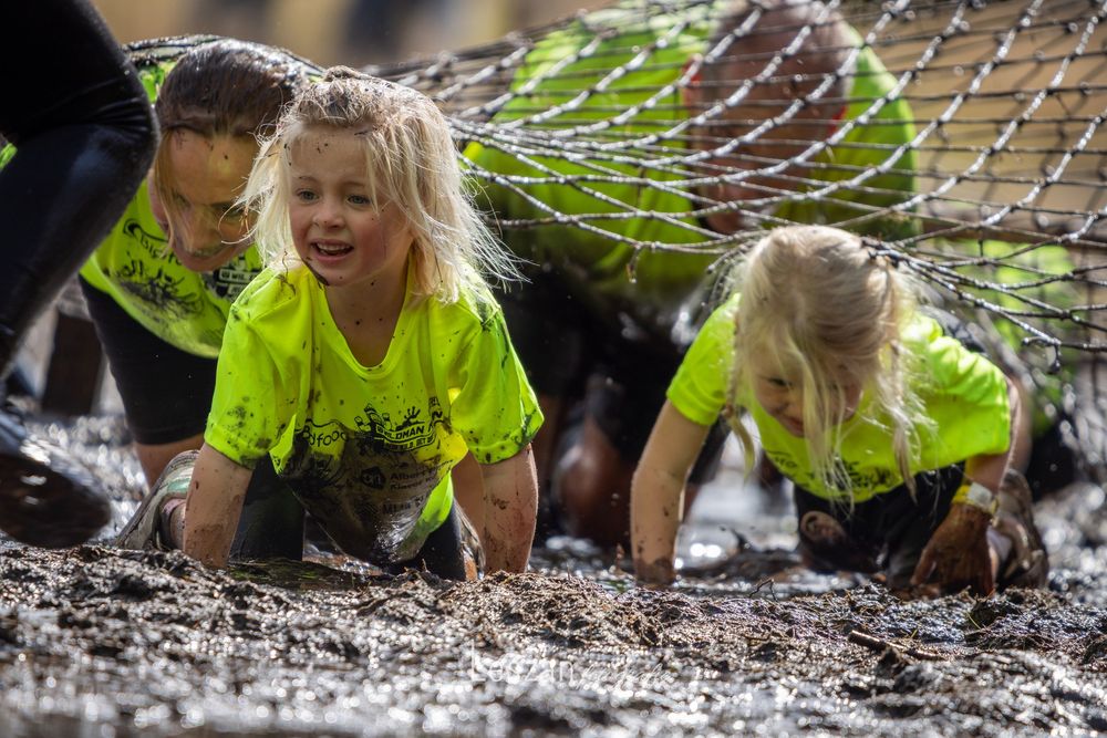 Participants crawl under low obstacles during a challenging outdoor mud run obstacle course race.