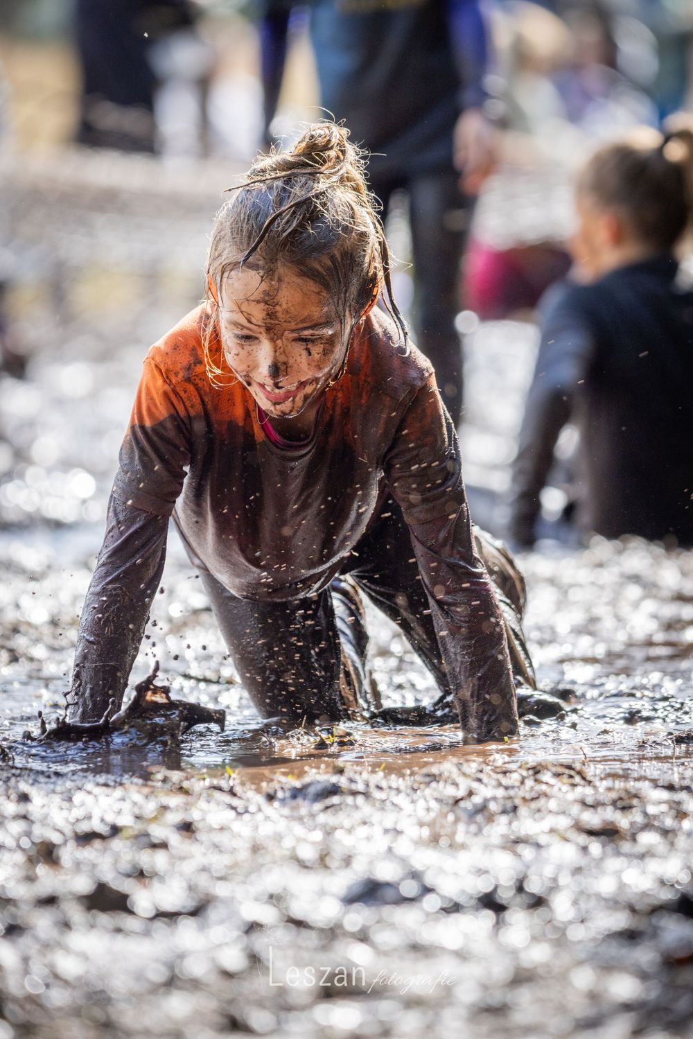 People crawling through deep brown mud on their hands and knees during a messy outdoor challenge.