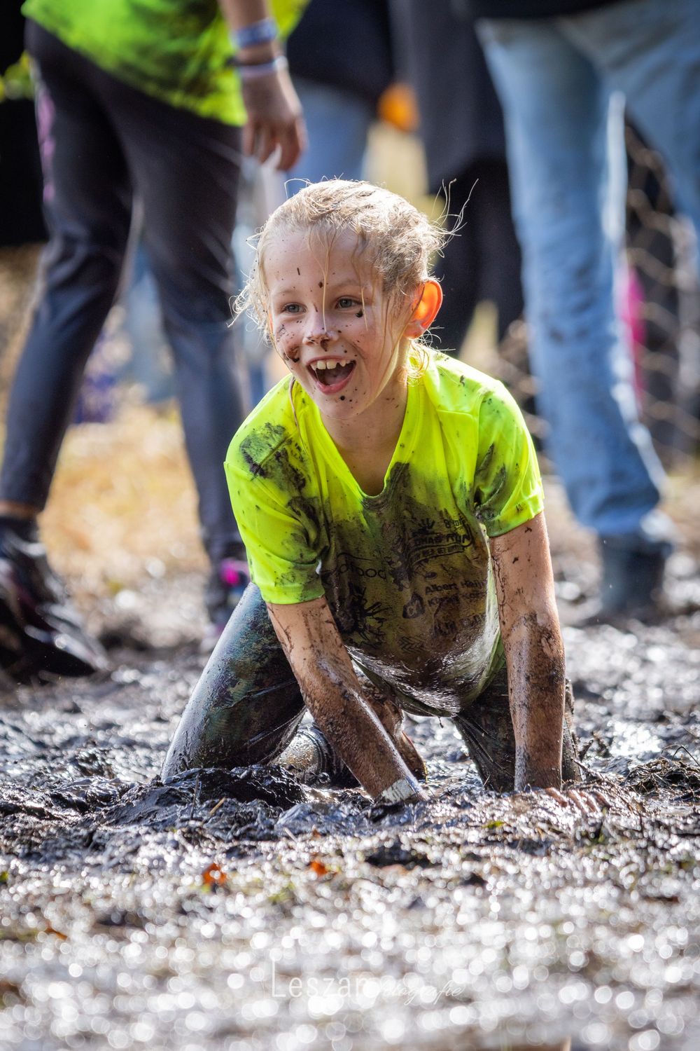 A sequence of photos showing a participant crawling and laughing through a muddy obstacle course wearing a neon yellow shirt.