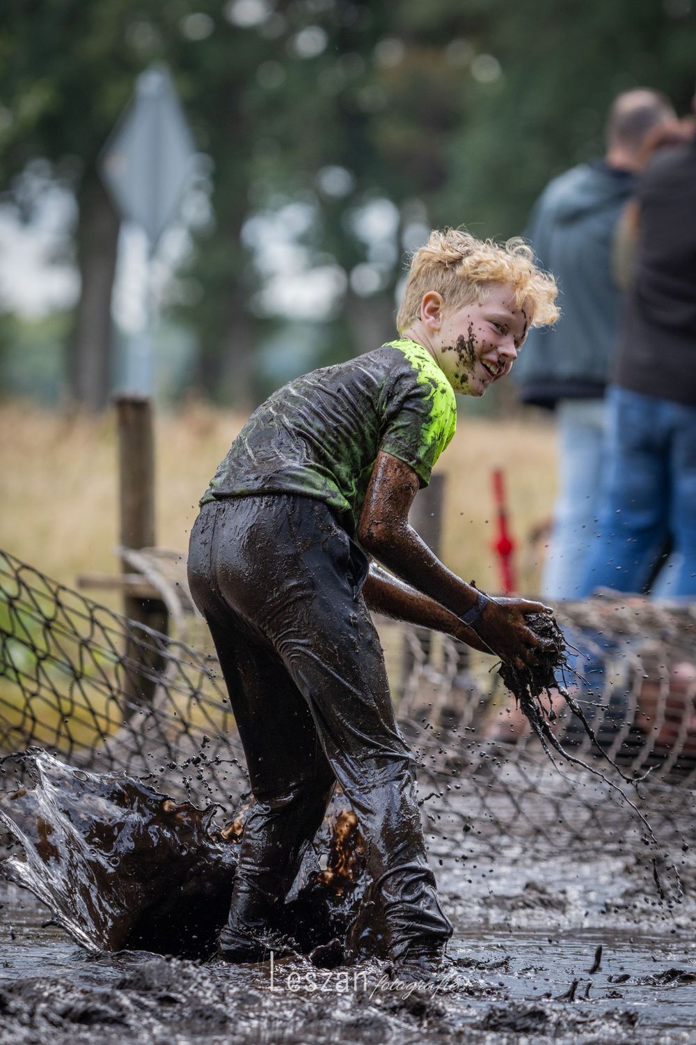 Multiple action shots of someone splashing through a muddy water obstacle while wearing a bright safety vest.