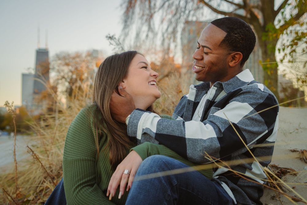 Autumn engagement photoshoot among willow trees with city backdrop.