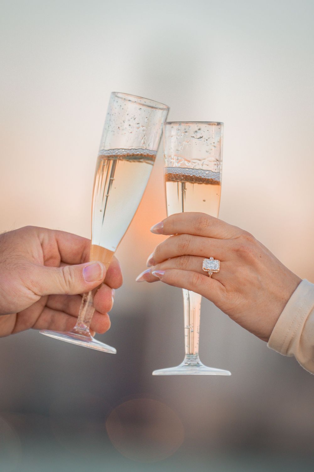 Champagne flutes clinking together with engagement ring visible in romantic celebration.