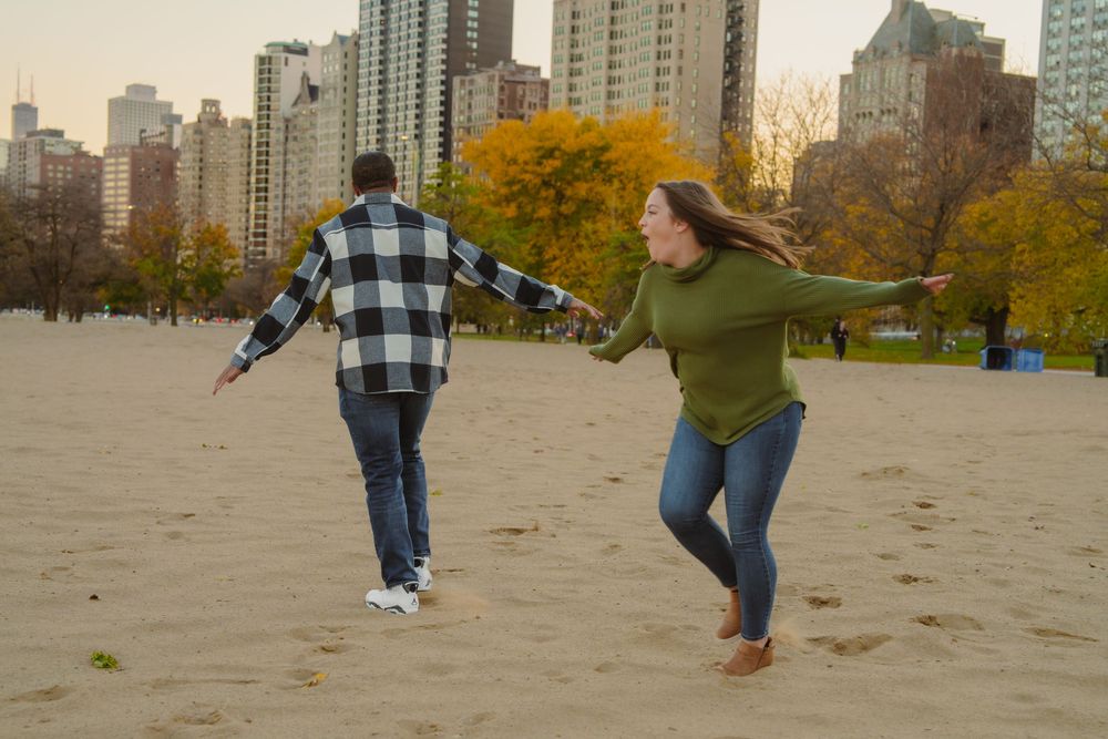 Playful couple walking and holding hands on sandy beach with fall foliage.
