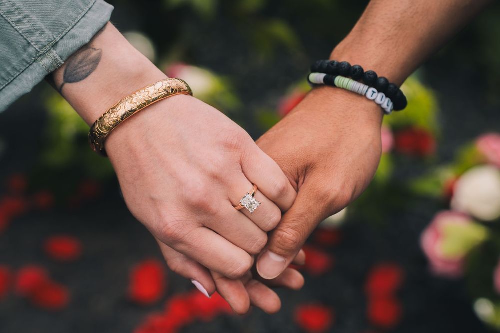 Close-up of hands with engagement rings against floral background.