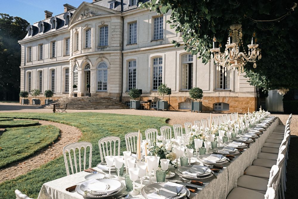 An elegant outdoor wedding reception table set in front of a grand French chateau with manicured lawns.