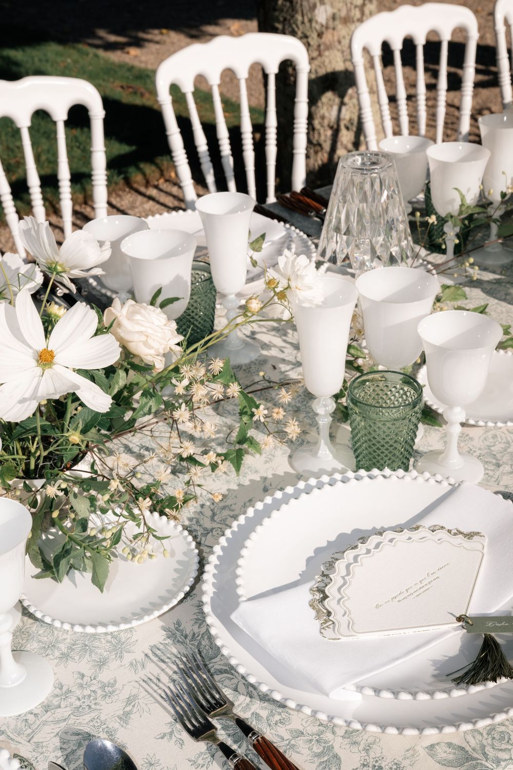 Elegant white table setting with beaded charger plates, green glassware and delicate floral arrangements for a wedding reception.