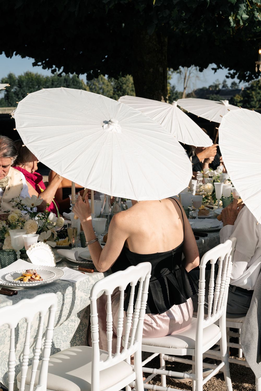 Guests seated at an outdoor dining event with white parasols shading them from above.