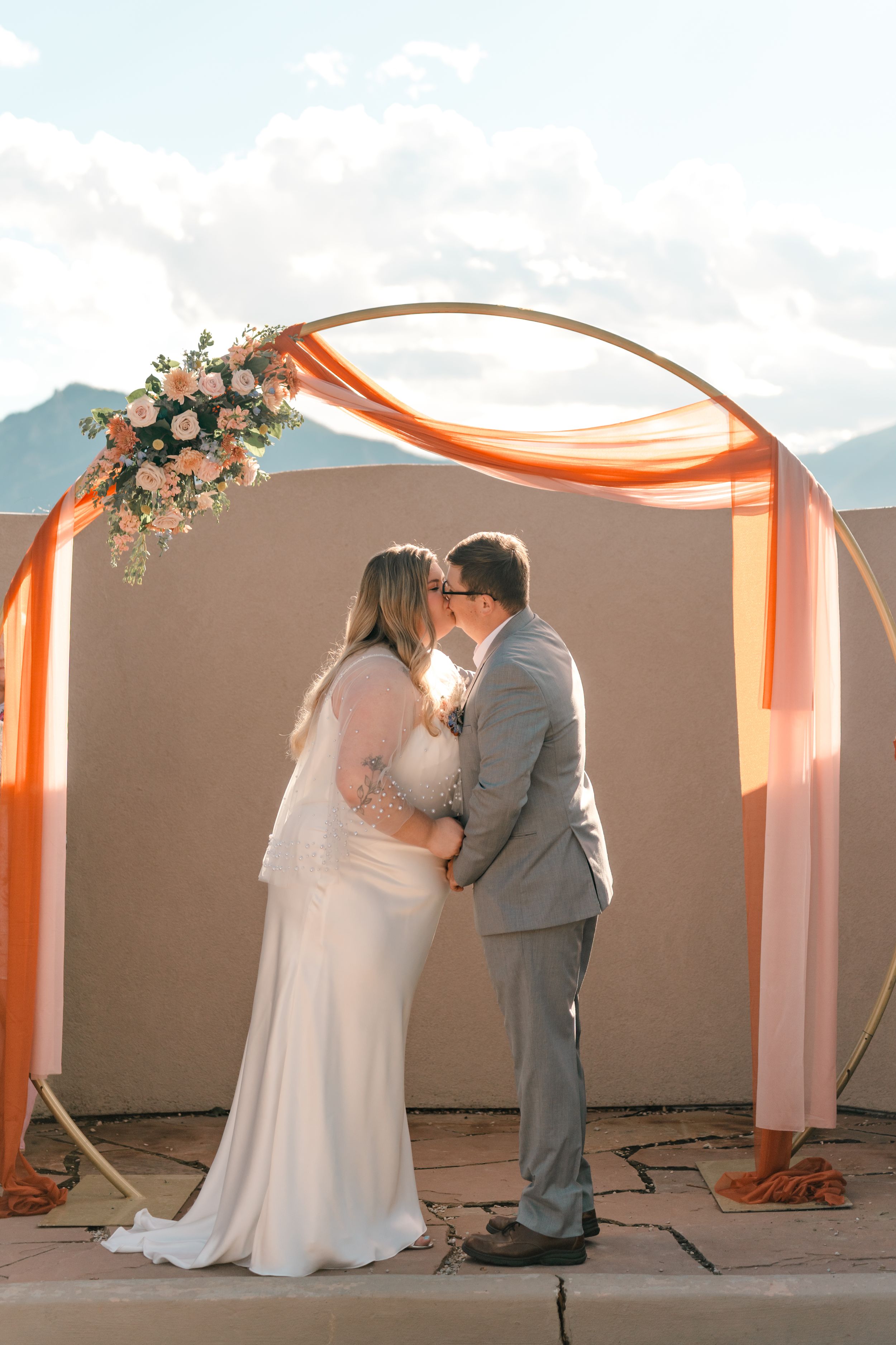A romantic wedding ceremony sequence shows a couple kissing under an orange-draped archway at sunset.
