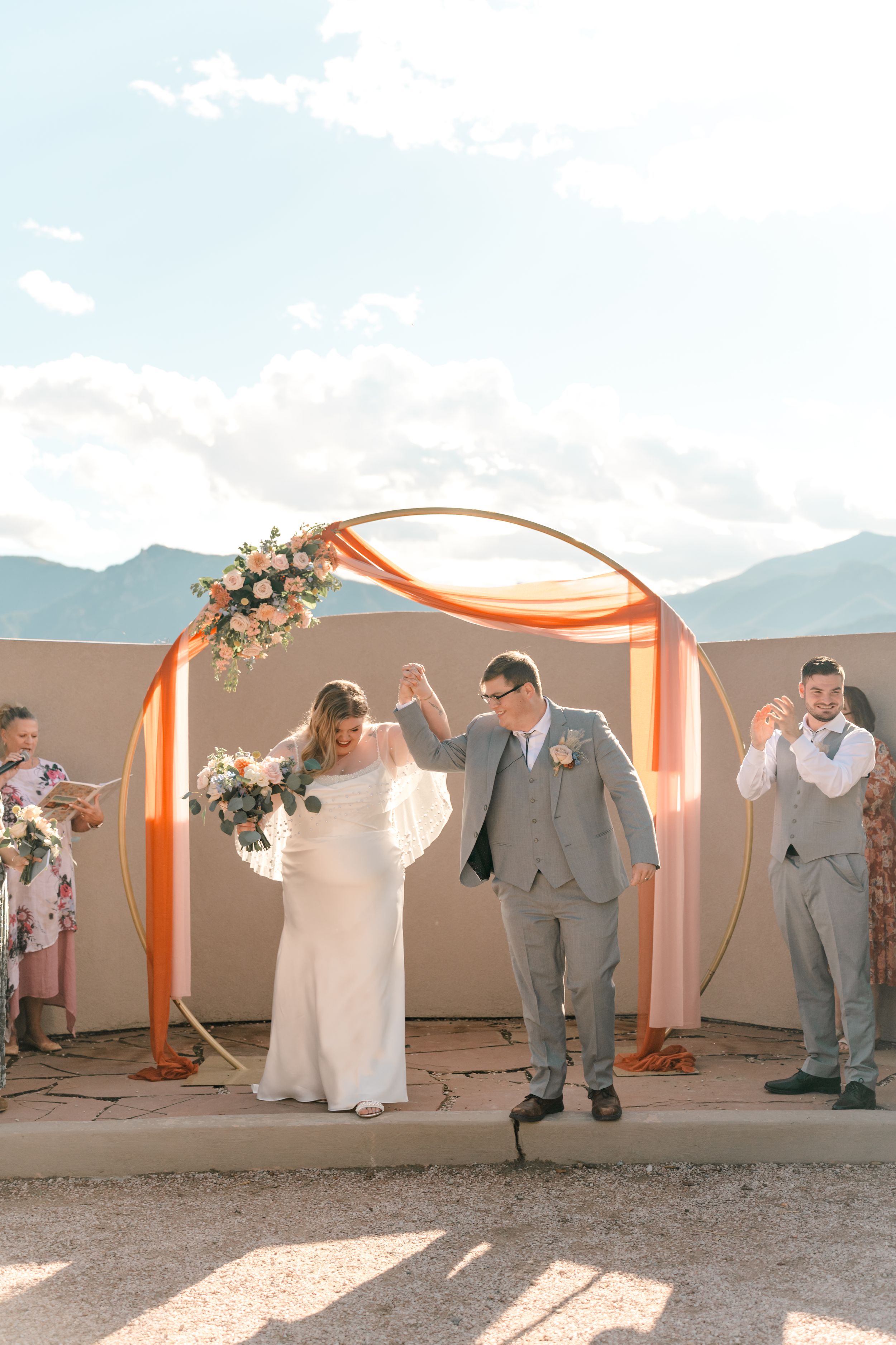 Wedding party poses playfully against an orange and white backdrop with mountains in the distance.
