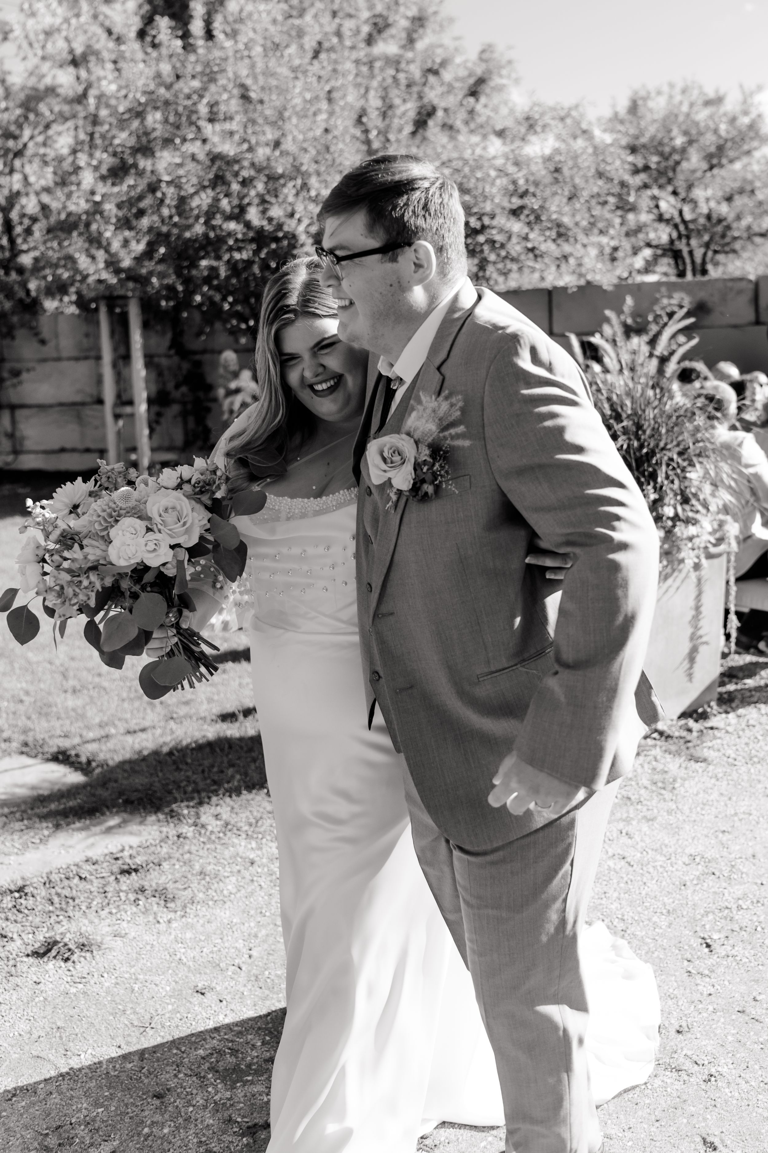 A couple shares romantic moments in a garden setting captured in black and white photography.