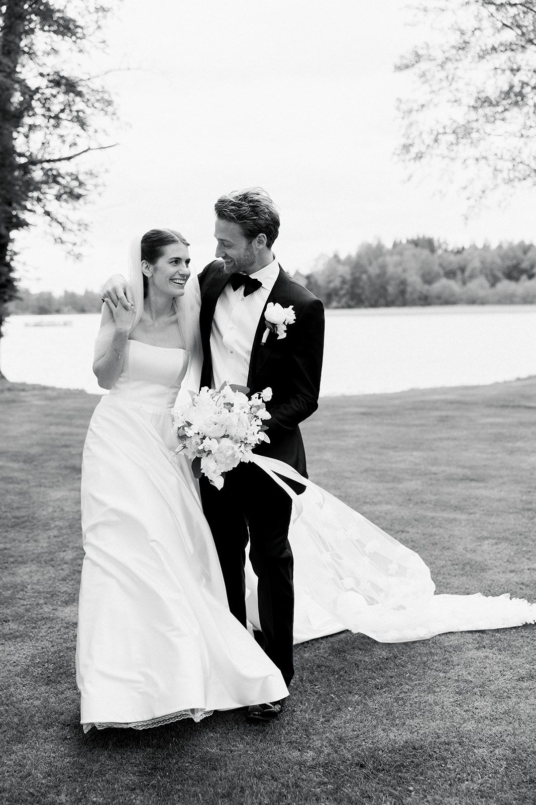A romantic black and white wedding photo series showing a couple dancing playfully on a grassy lawn.