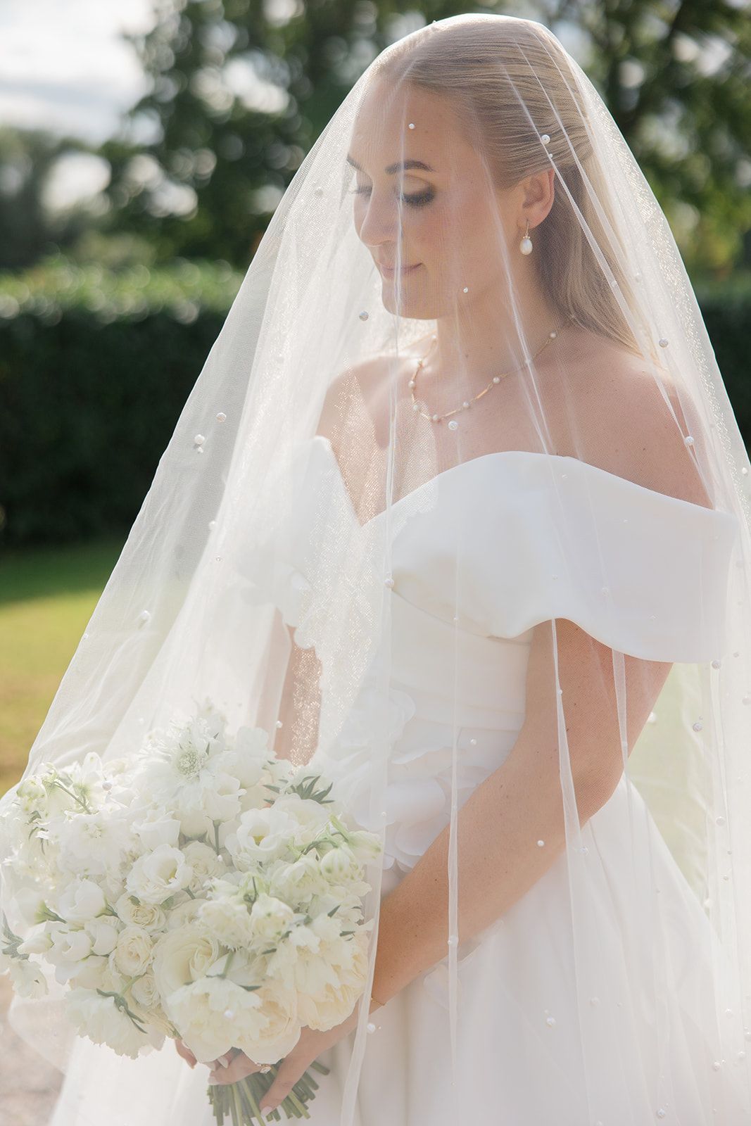 A romantic black and white wedding photo of a couple outdoors, with the bride in a flowing white gown looking back at camera.