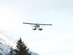 Small aircraft flying over snow-capped mountains in pristine wilderness terrain.