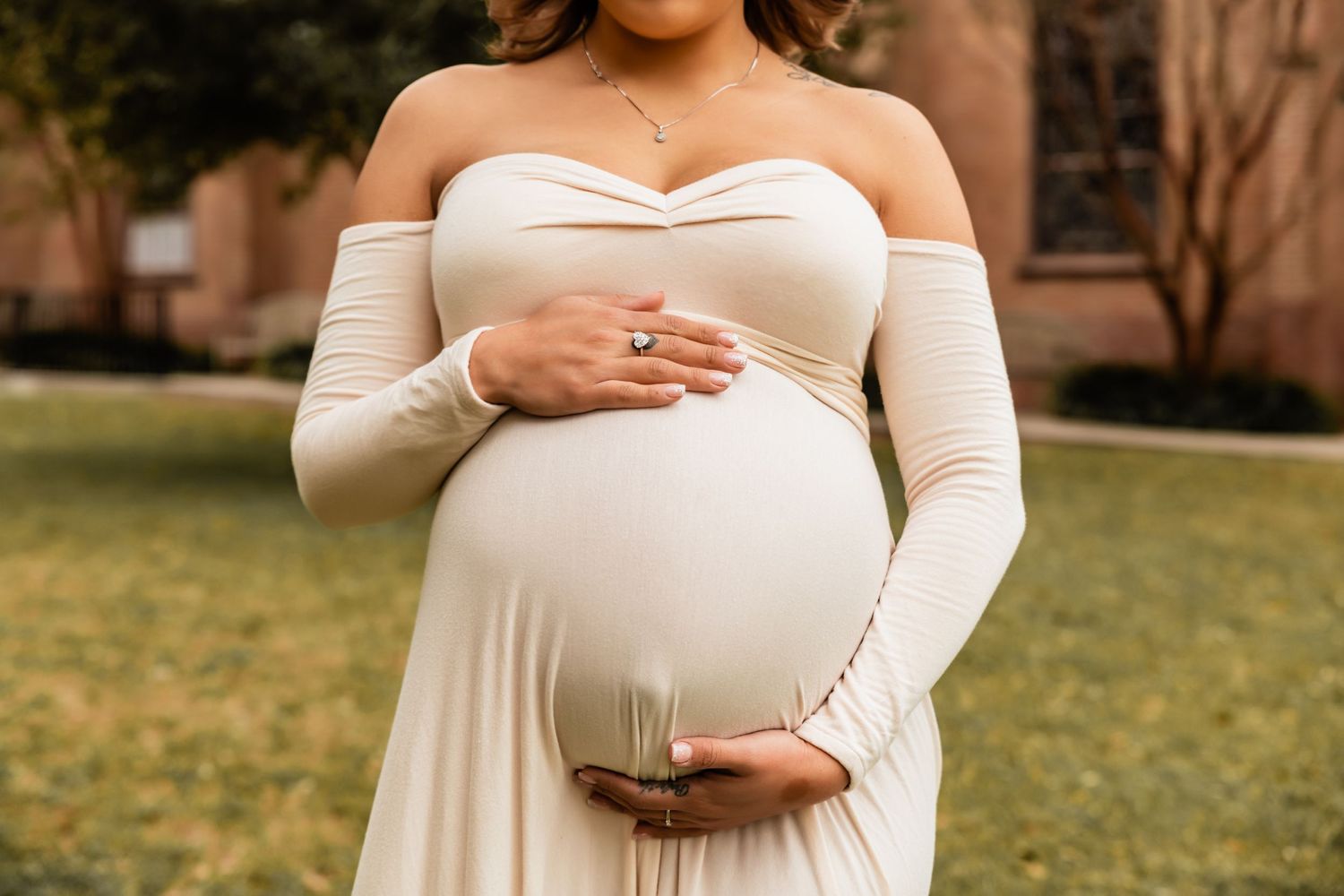 Close-up of a pregnant woman's belly in a white off-shoulder dress showing her engagement ring.