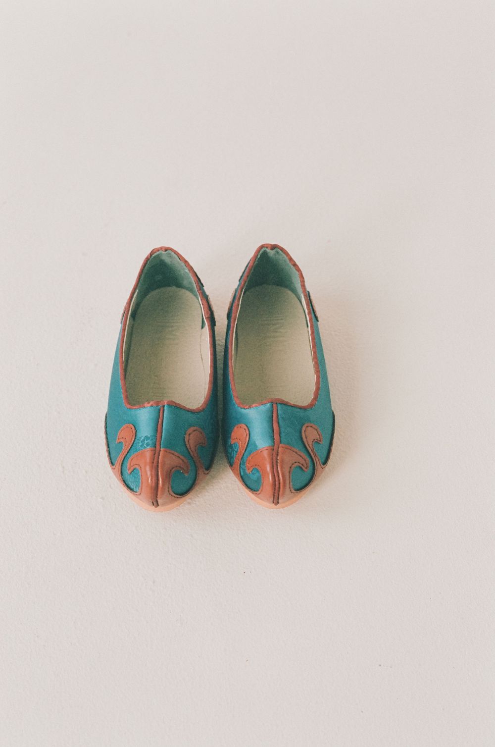 Tiny teal and coral baby shoes displayed in different angles on a white background.