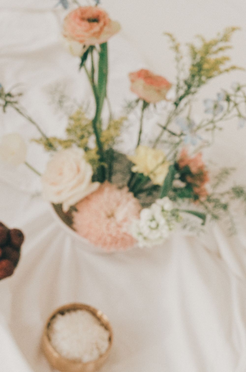 Delicate peach roses and white baby's breath flowers arranged in a small vase on a white tablecloth.