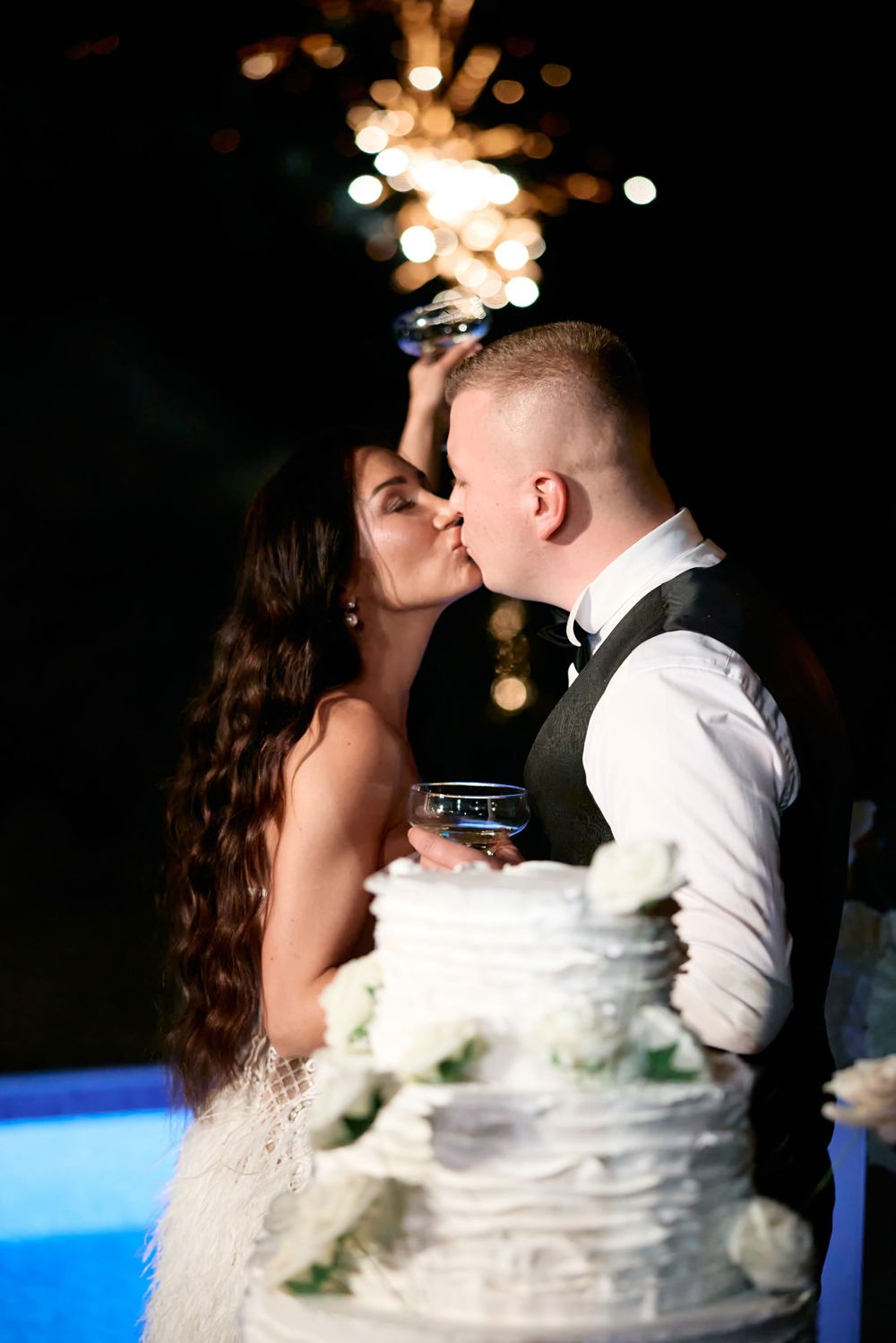 A couple shares an intimate moment during their wedding reception while standing near a white wedding cake.