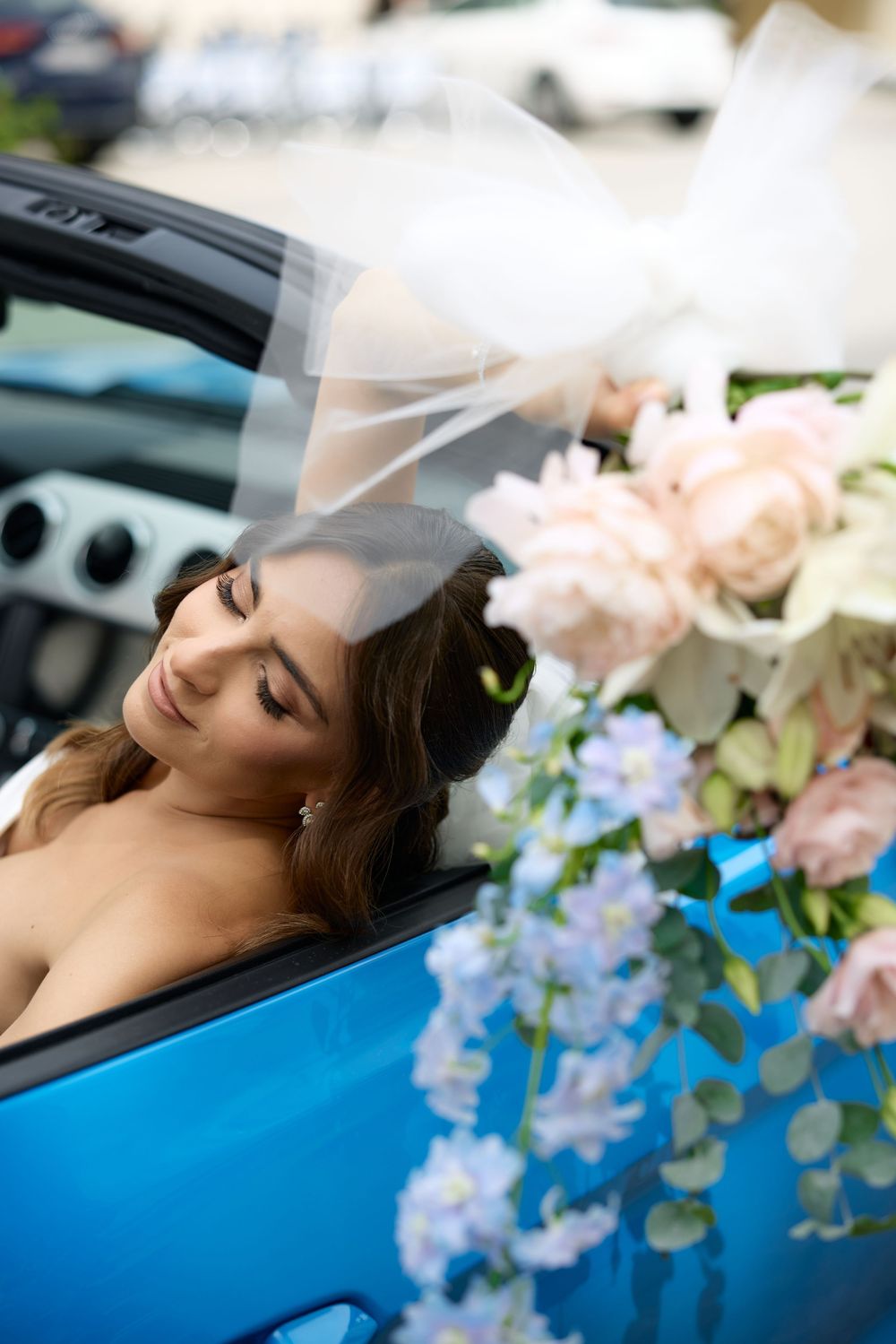 Romantic bridal portraits with delicate flowers and soft lighting against blue car interior.