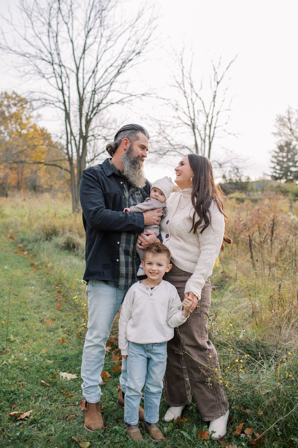 A family enjoys a playful moment together in an autumn field with tall grass and trees in the background.