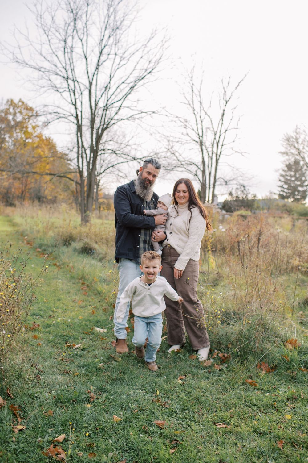 A family plays together on a grassy hillside during autumn with bare trees in the background.