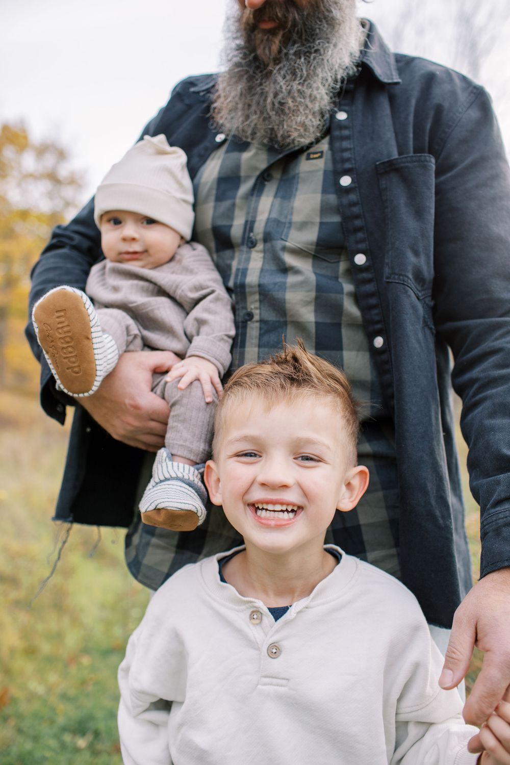 A family poses together outdoors during an autumn photoshoot with fall foliage in the background.