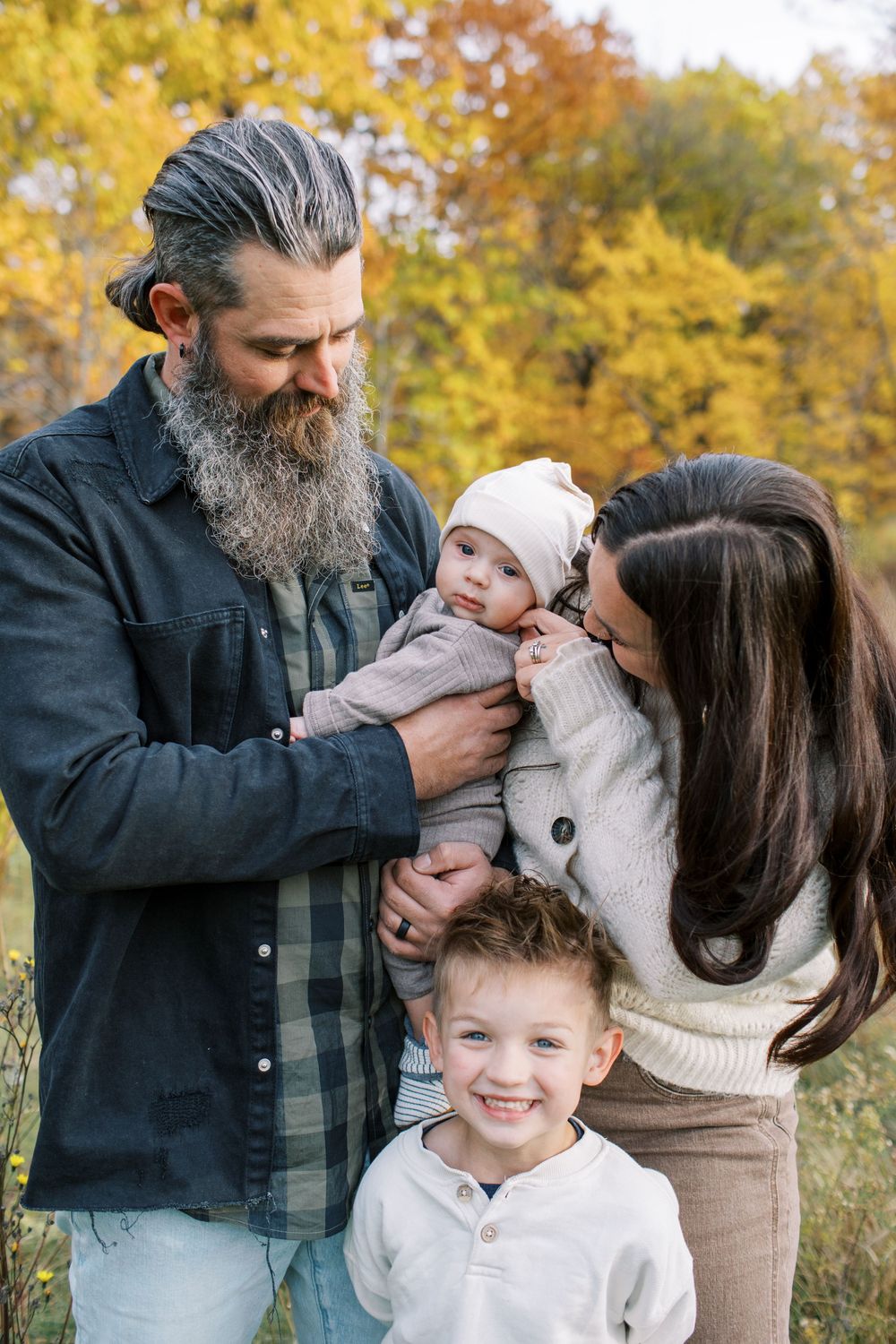 A sweet family moment captured in autumn with yellow foliage in the background as they embrace and share affection.
