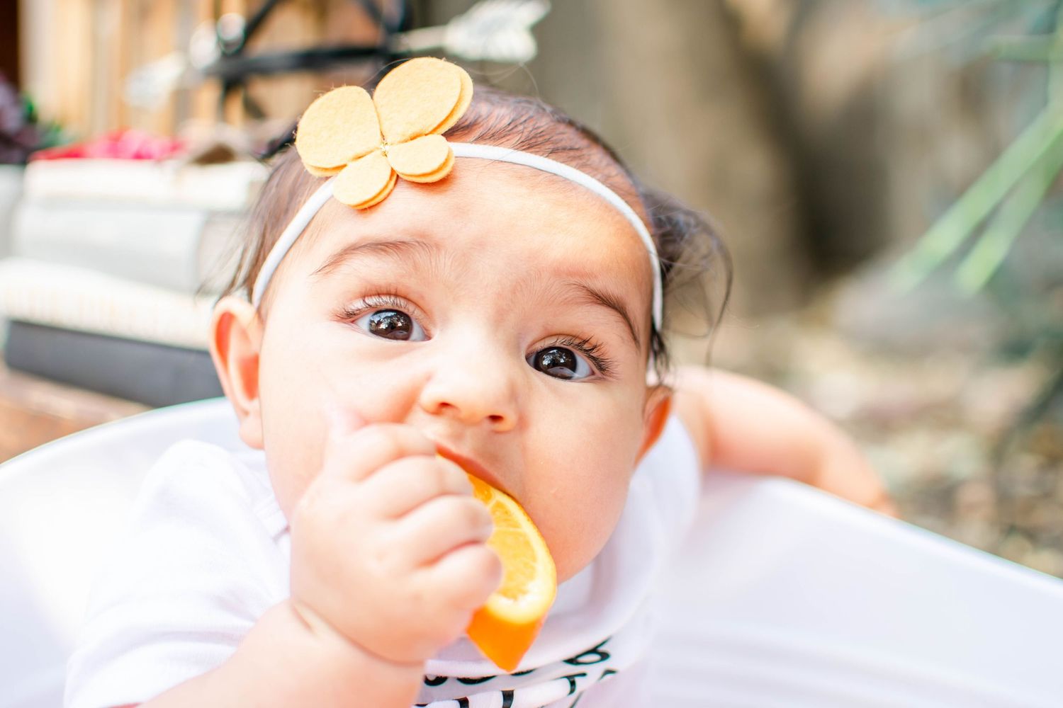 Baby in high chair enjoys eating orange fruit puree during mealtime.
