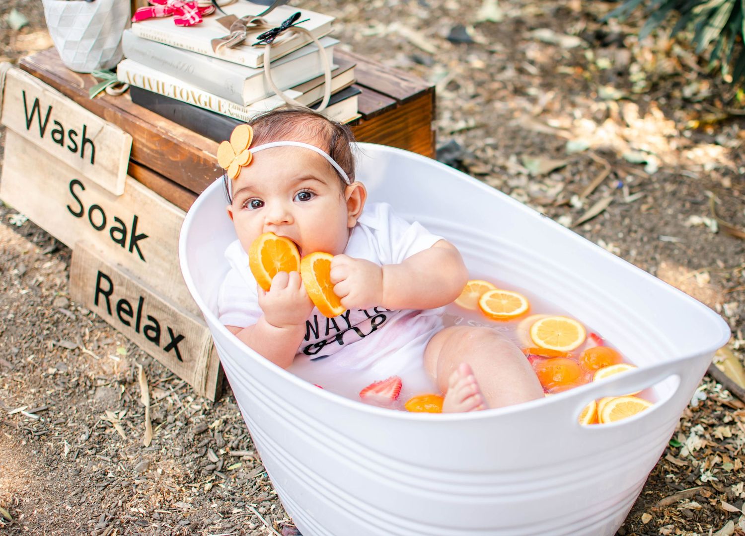 A small figure relaxes in a white tub filled with water and orange citrus slices during an outdoor bath.