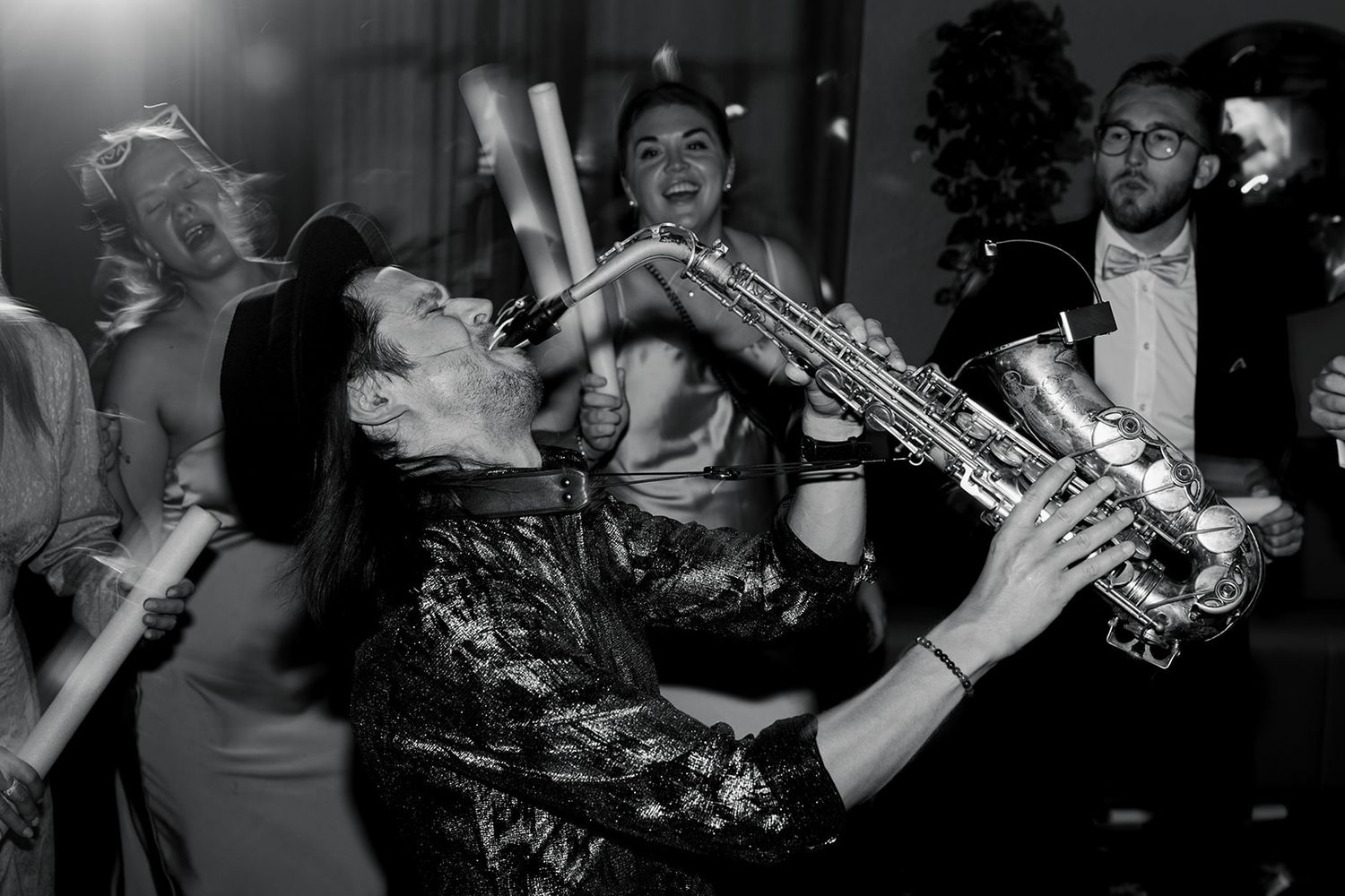 A saxophone player performs energetically in black and white at a lively nightclub event.