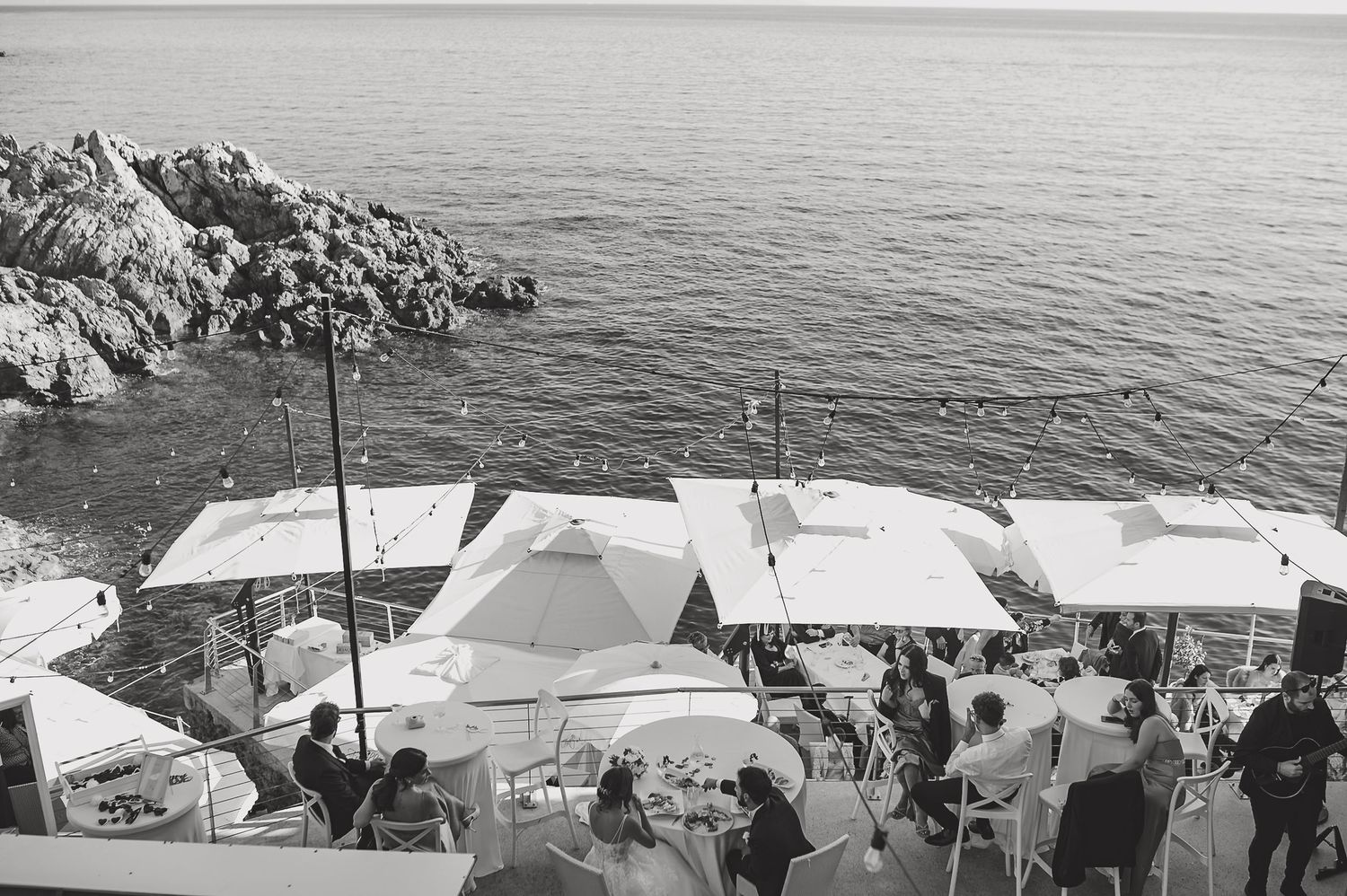 Una veduta panoramica in bianco e nero di una costa rocciosa con tende e persone radunate vicino alla riva.