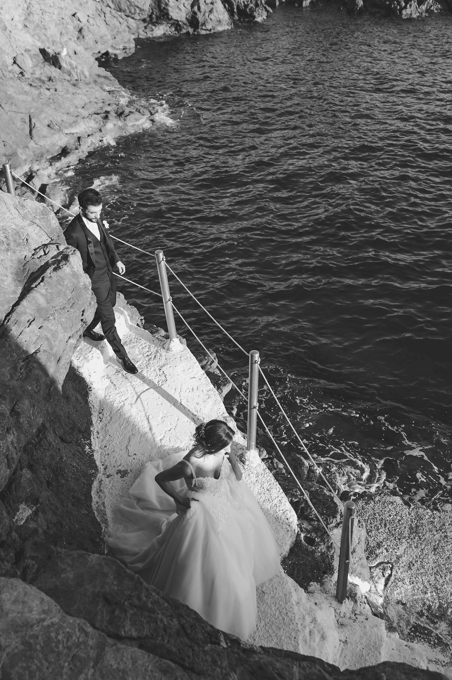Una coppia in abiti da cerimonia nuziale posa in modo teatrale sulle scogliere costiere che si affacciano sulle scure acque dell'oceano.