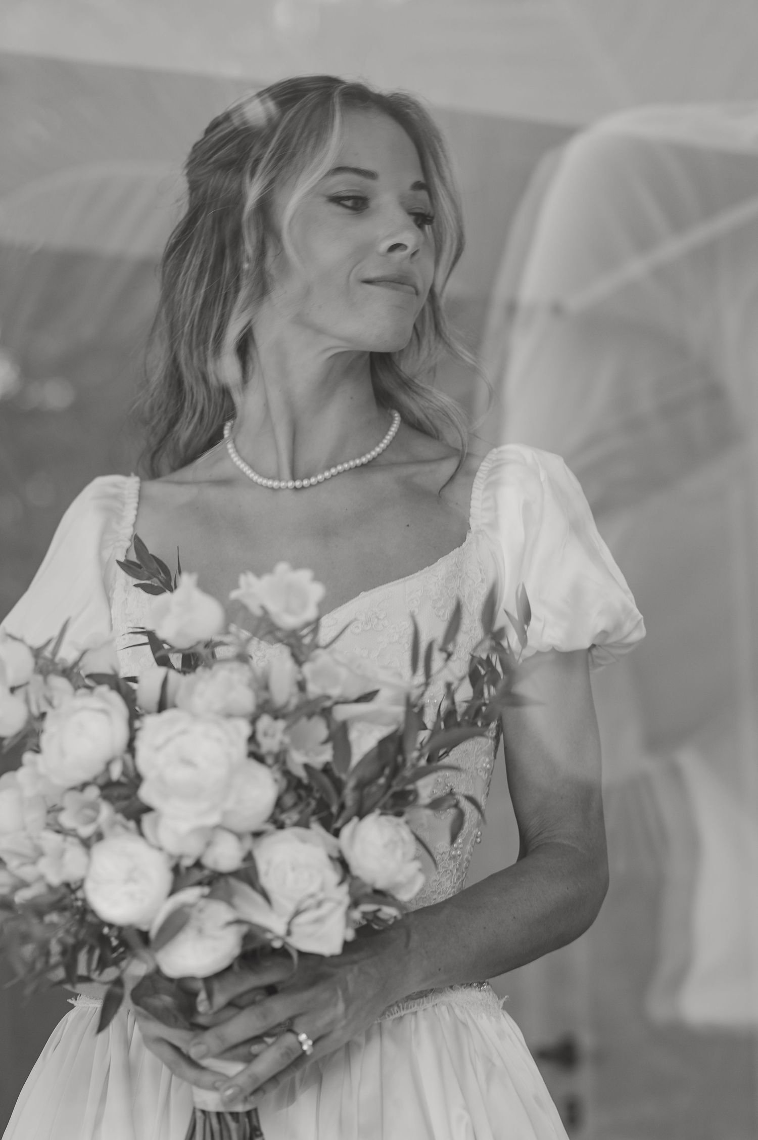 Ritratto in bianco e nero di una sposa con un abito da sposa a maniche a sbuffo che tiene in mano un romantico bouquet di rose e fiori.