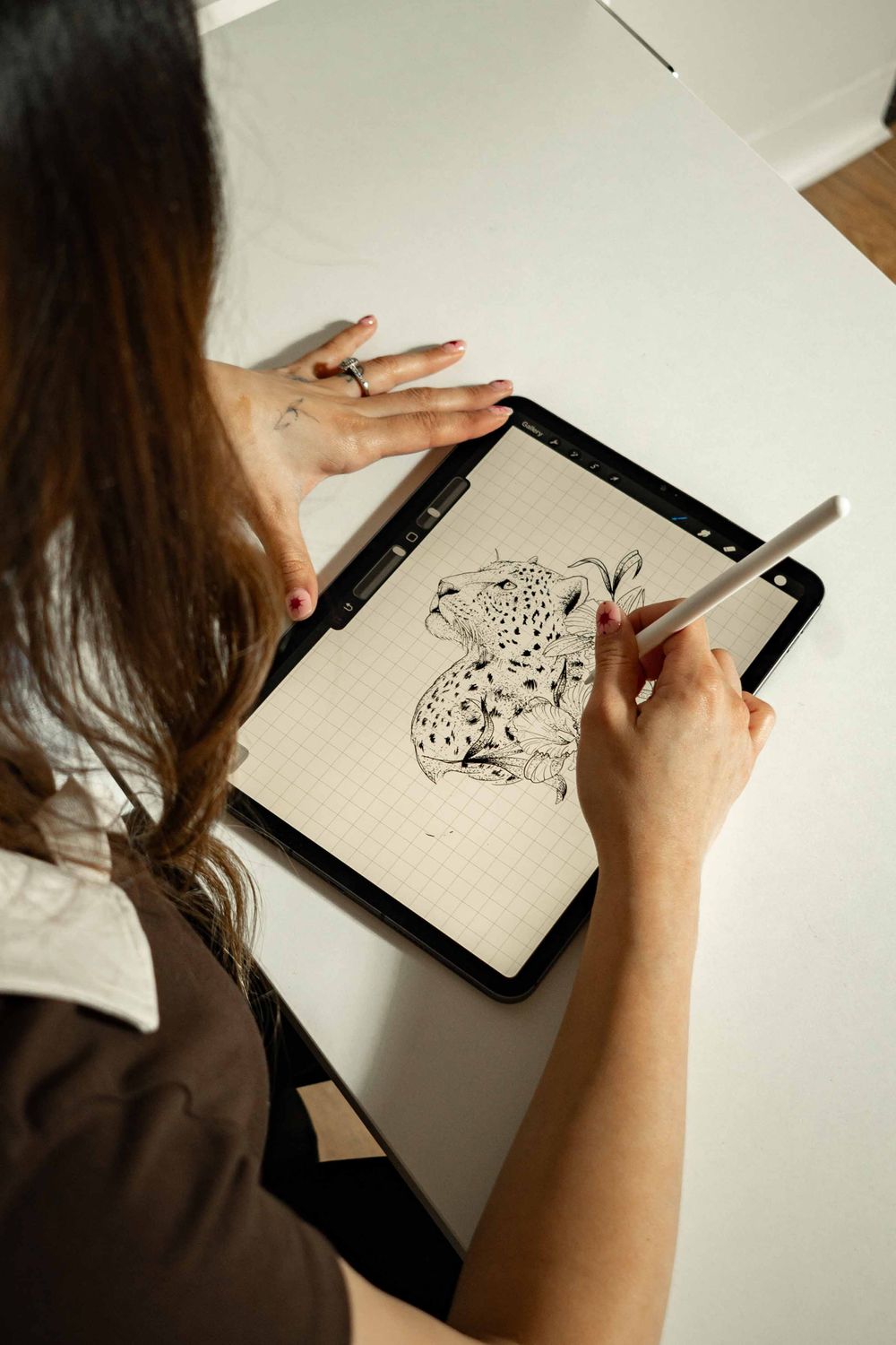 Woman drawing a detailed leopard illustration on a digital tablet using a stylus pen at a white desk.