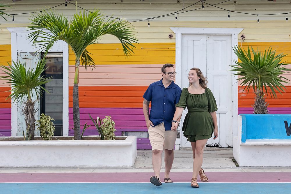 Couple walking hand in hand by colorful rainbow mural in Isla Mujeres.