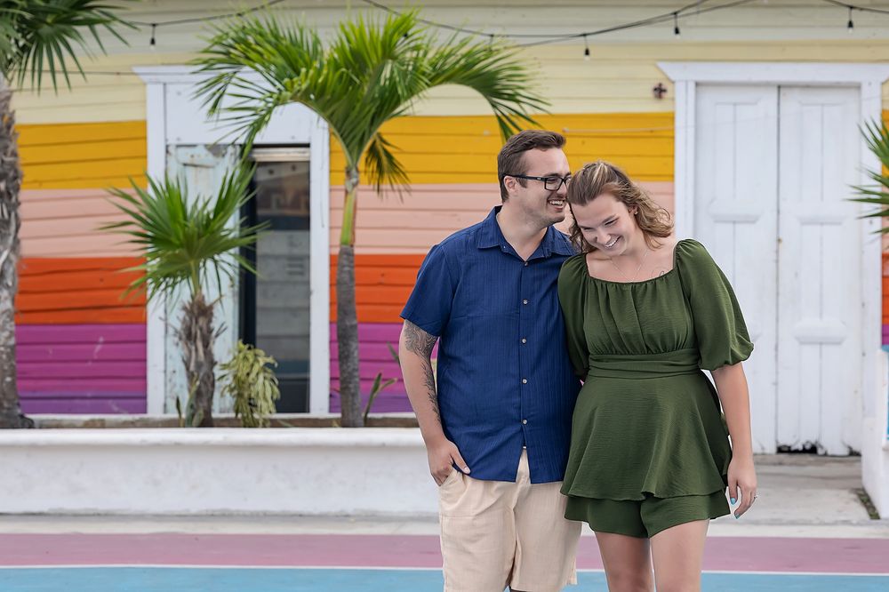 A couple embraces while standing in front of a colorful striped wall with palm trees.