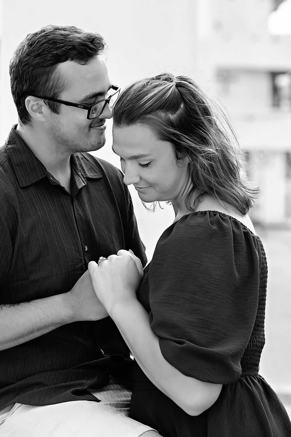 Intimate black and white portrait of couple holding hands and leaning close.
