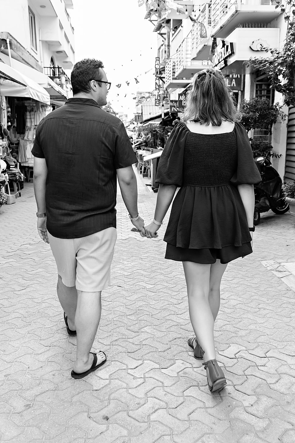 A couple walking together down a paved path shown from behind in black and white.