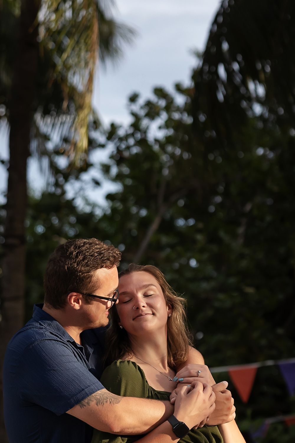 A tender moment between a couple at dusk with tropical foliage silhouetted behind them.