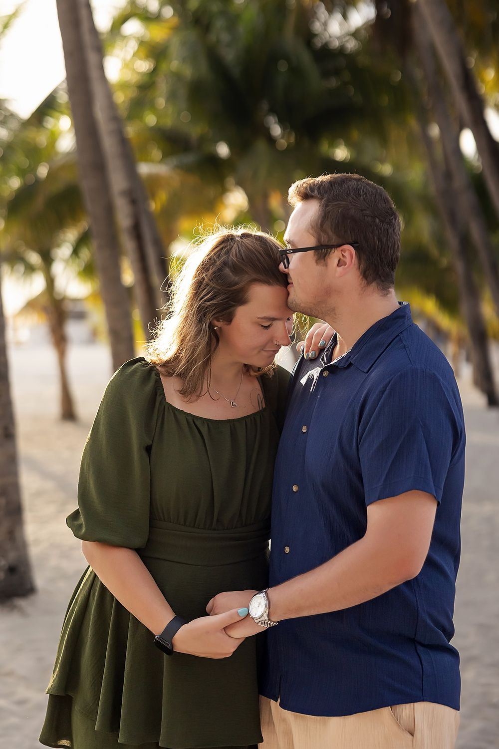 A romantic couple embracing at sunset with palm trees in the background.