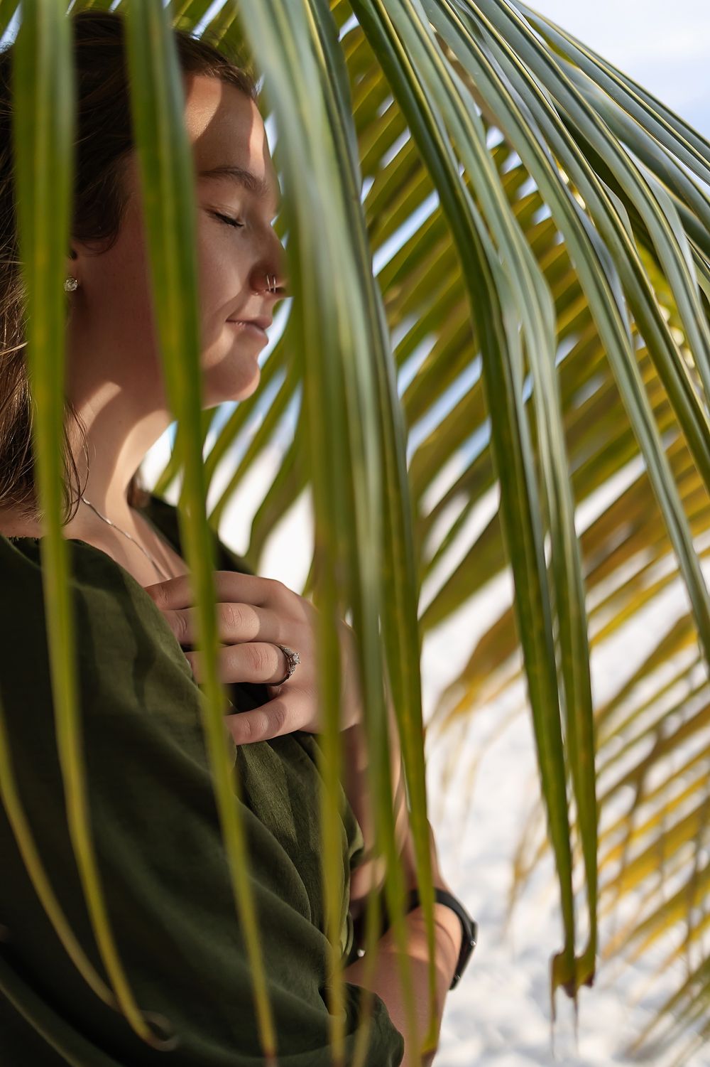 Woman framed by palm leaves with engagement ring visible.