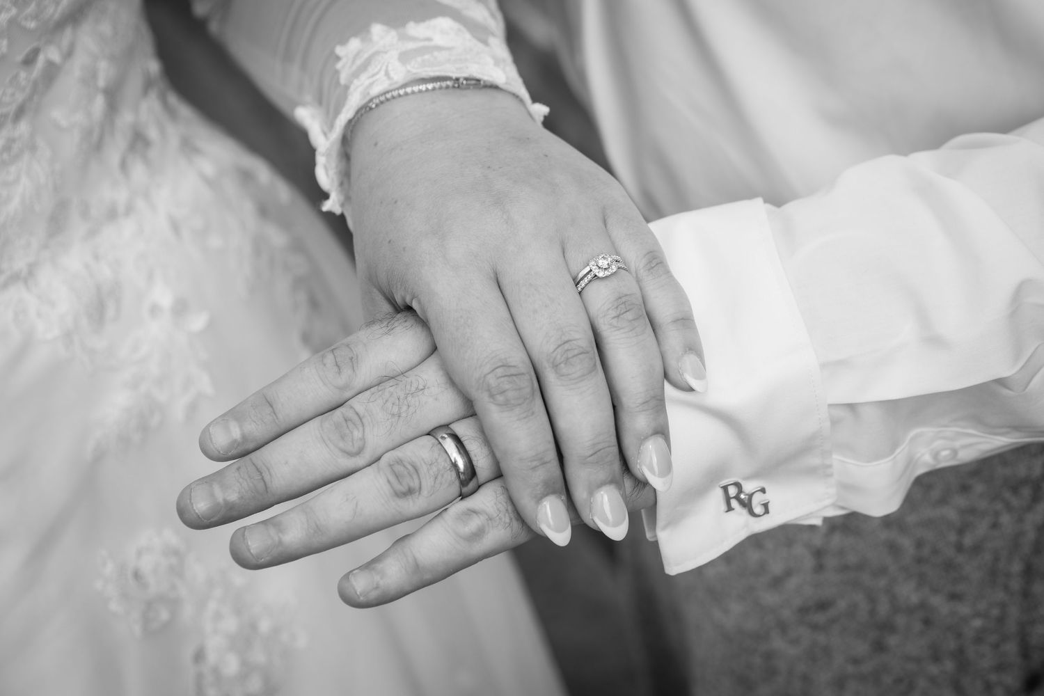 Black and white close-up of hands with wedding rings showing newlywed couple's first intimate moment together.