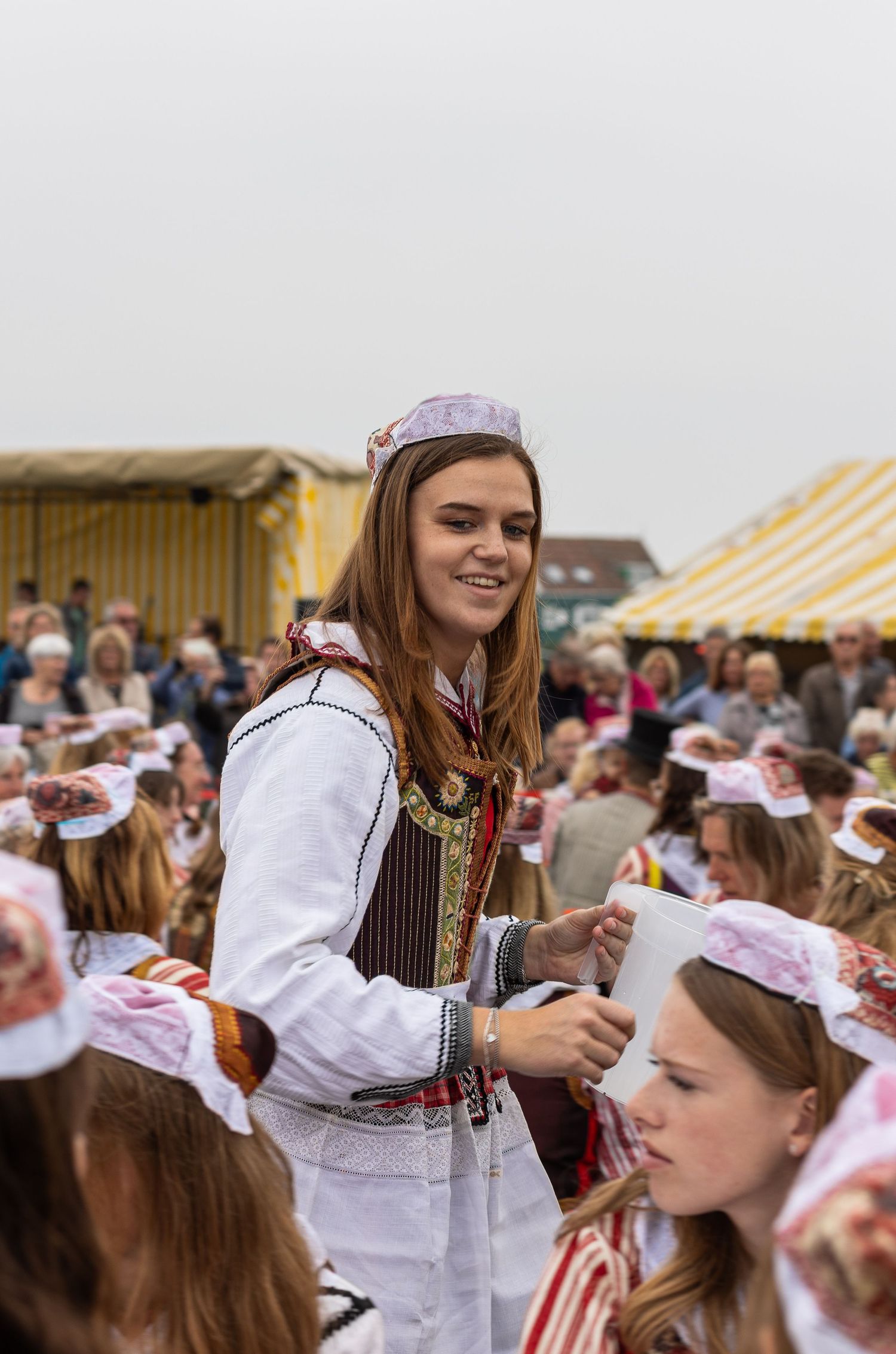 People in traditional Estonian folk costumes gather at a cultural festival under striped tents.