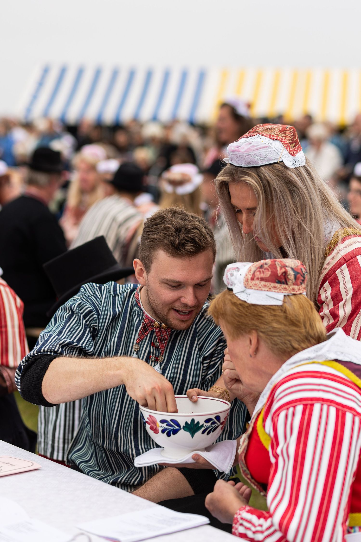 People in traditional Estonian clothing share a meal at outdoor tables during a cultural festival.