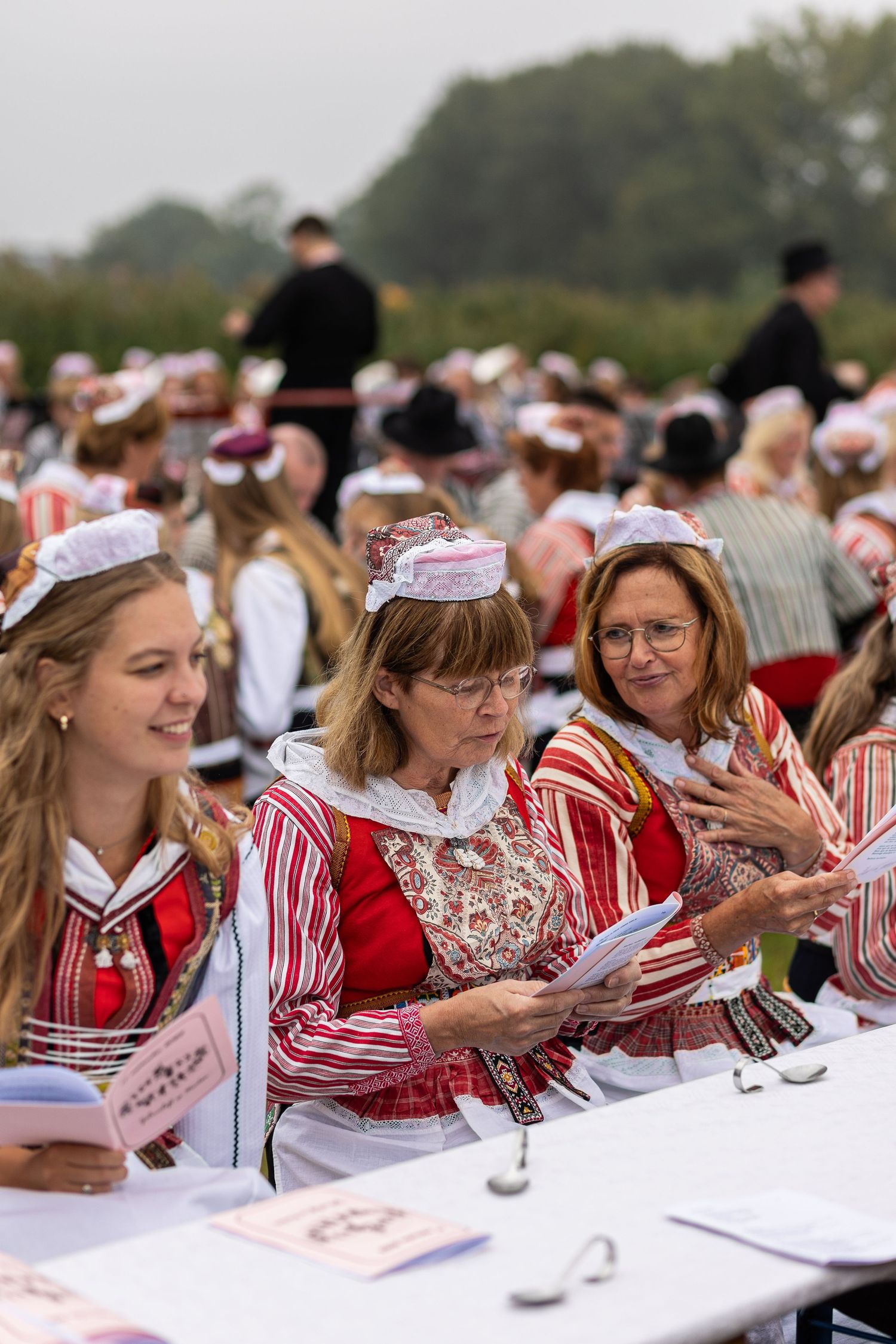 Students in traditional red and white attire sit at long tables during a formal academic event.