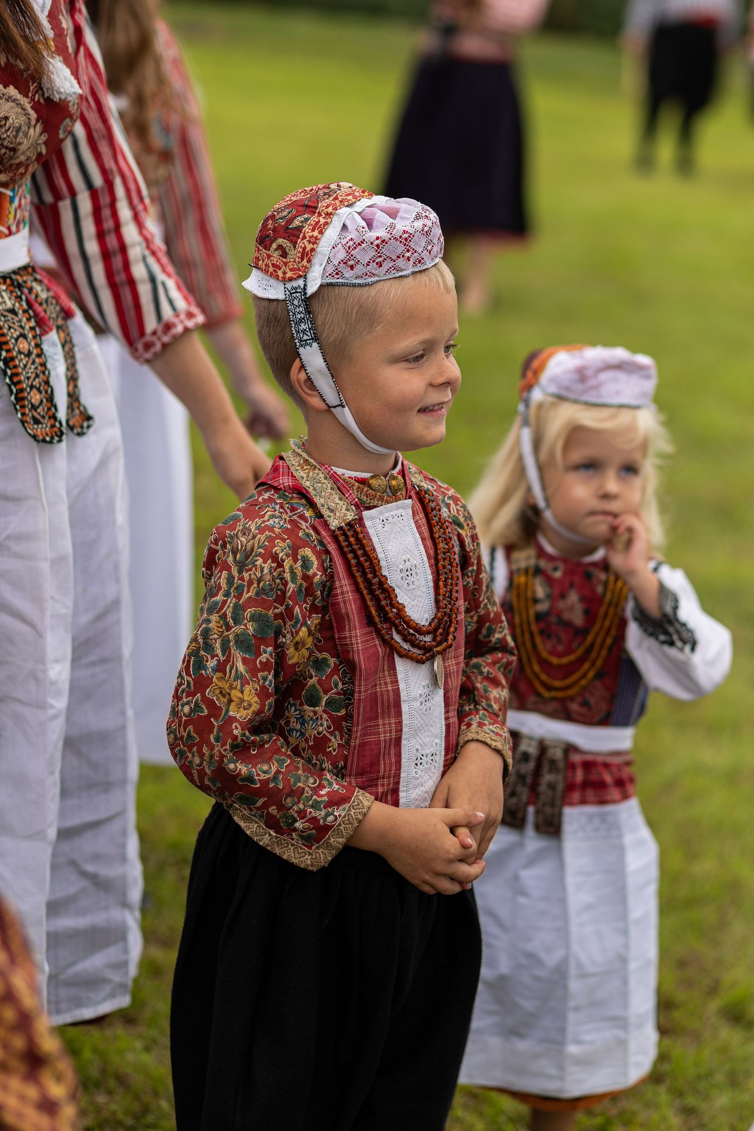 Children in traditional Estonian folk costumes perform a dance at an outdoor cultural celebration.